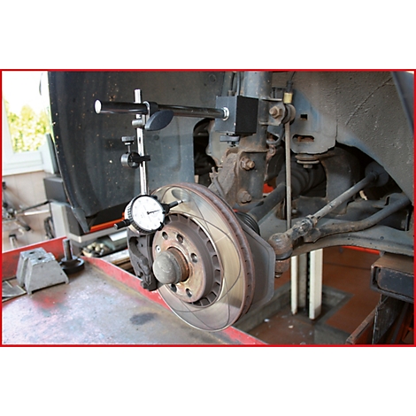 Nahaufnahme der Bremsscheibe eines Autos in einer Werkstatt mit Messwerkzeug zur Diagnose.